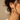 A close-up side profile of a woman wearing a colorful floral drop earring with gold-toned hooks against a warm beige background.