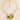 A gold chain necklace with paperclip-style links and a cluster of ceramic charms, including a yellow lemon, green leaves, a white flower with green leaves, and a small white oval charm, displayed on a light beige background.