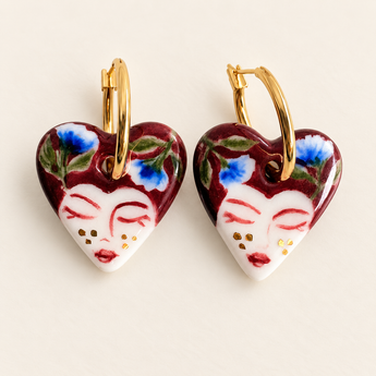 Close-up of blue flowers, burgundy brushwork and gold lustre accents on a porcelain portrait heart earring.