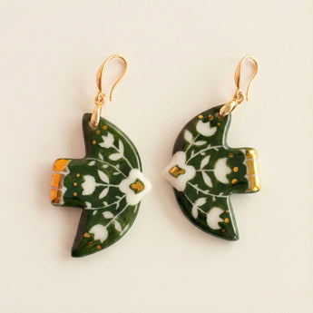 Green leaf-shaped earrings with white floral patterns on a beige background