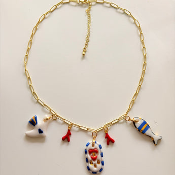 Gold paperclip chain necklace with hand-painted ceramic dove, coral, fish, and medallion charms, laid flat