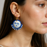 Celestial Gaze Porcelain Earrings in cobalt blue with 22k gold accents depicted on a model's ear, showcasing unique statement earrings that feature expressive moon faces.