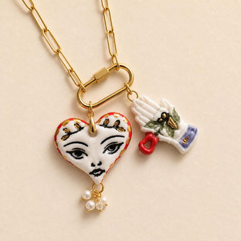 Porcelain heart pendant hand-painted with a feminine face, gold leaf crown accents, and a small hand-and-rose charm, on a gold paperclip chain