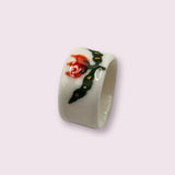 A handmade white porcelain ring featuring a vibrant hand-painted red tulip with green leaves and small gold accents. The ring has a smooth, glossy finish and a wide band. Its minimalist design and floral detailing create an elegant look.