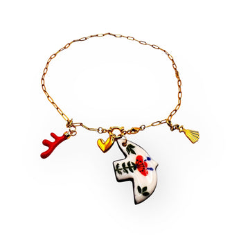 A handmade gold chain bracelet featuring unique charms: a ceramic bird-shaped pendant with hand-painted red and green floral details, a red coral-shaped charm, a small gold heart, and a gold seashell. The bracelet has a lightweight and artistic