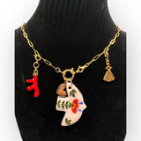 A handmade gold chain bracelet featuring unique charms: a ceramic bird-shaped pendant with hand-painted red and green floral details, a red coral eshaped charm, a small gold heart, and a gold seashell. The bracelet has a lightweight and artistic desi